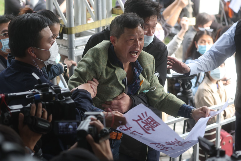 台灣國理事長陳峻涵(中綠衣者)持 標語到場抗議,遭現場人員拉住制止。 中央社