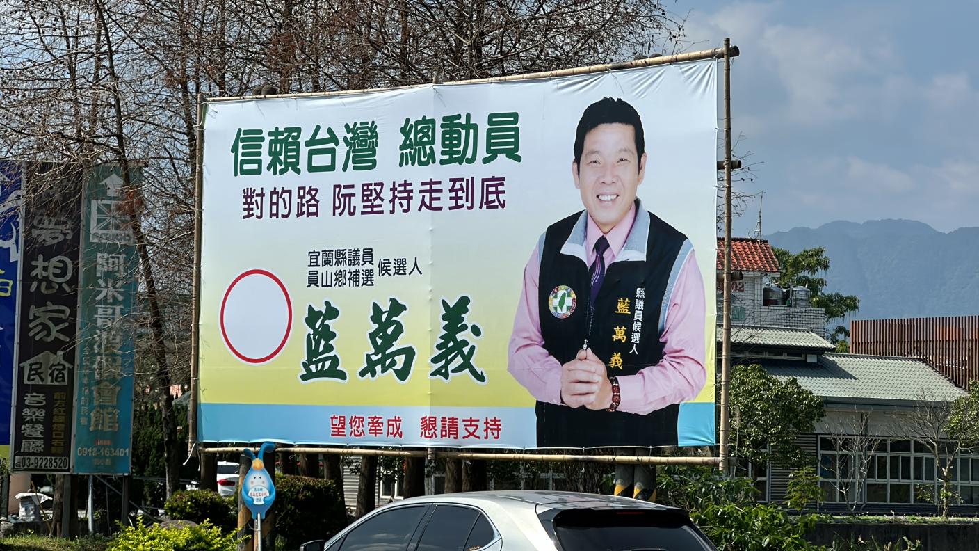 民進黨宜蘭縣員山鄉議員補選人選紛爭，負責協調的鄉代會主席許芳明心臟病發20日辭世，有意參選的前鄉代藍萬義今換上廣告看板，上頭寫「對的路阮堅持走到底」，參選態勢相當明確。林泊志攝