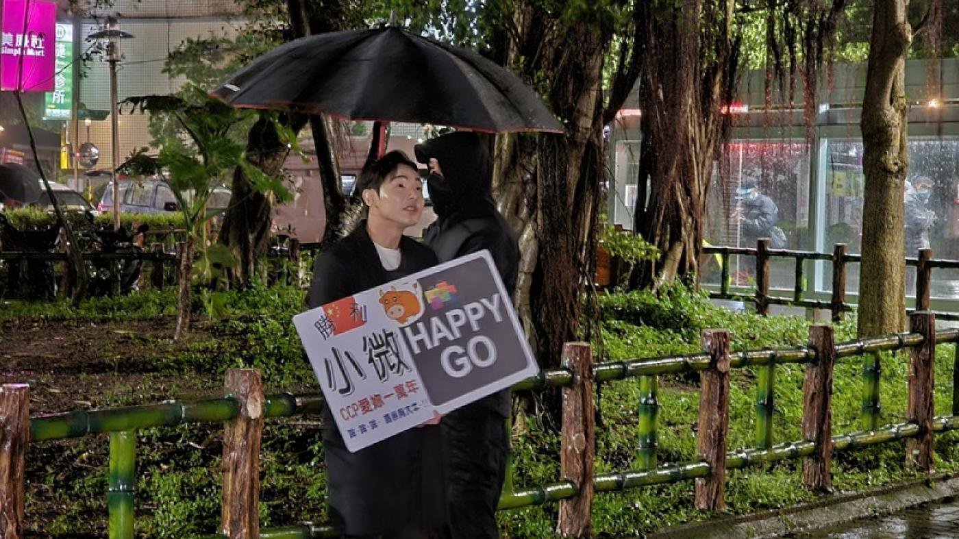 中配「小微」因發布影片涉鼓吹武統言論，遭移民署廢止居留許可，限期昨（31日）前離境，網紅八炯（舉牌者）晚間特地到其住處前舉牌送行。 中央社