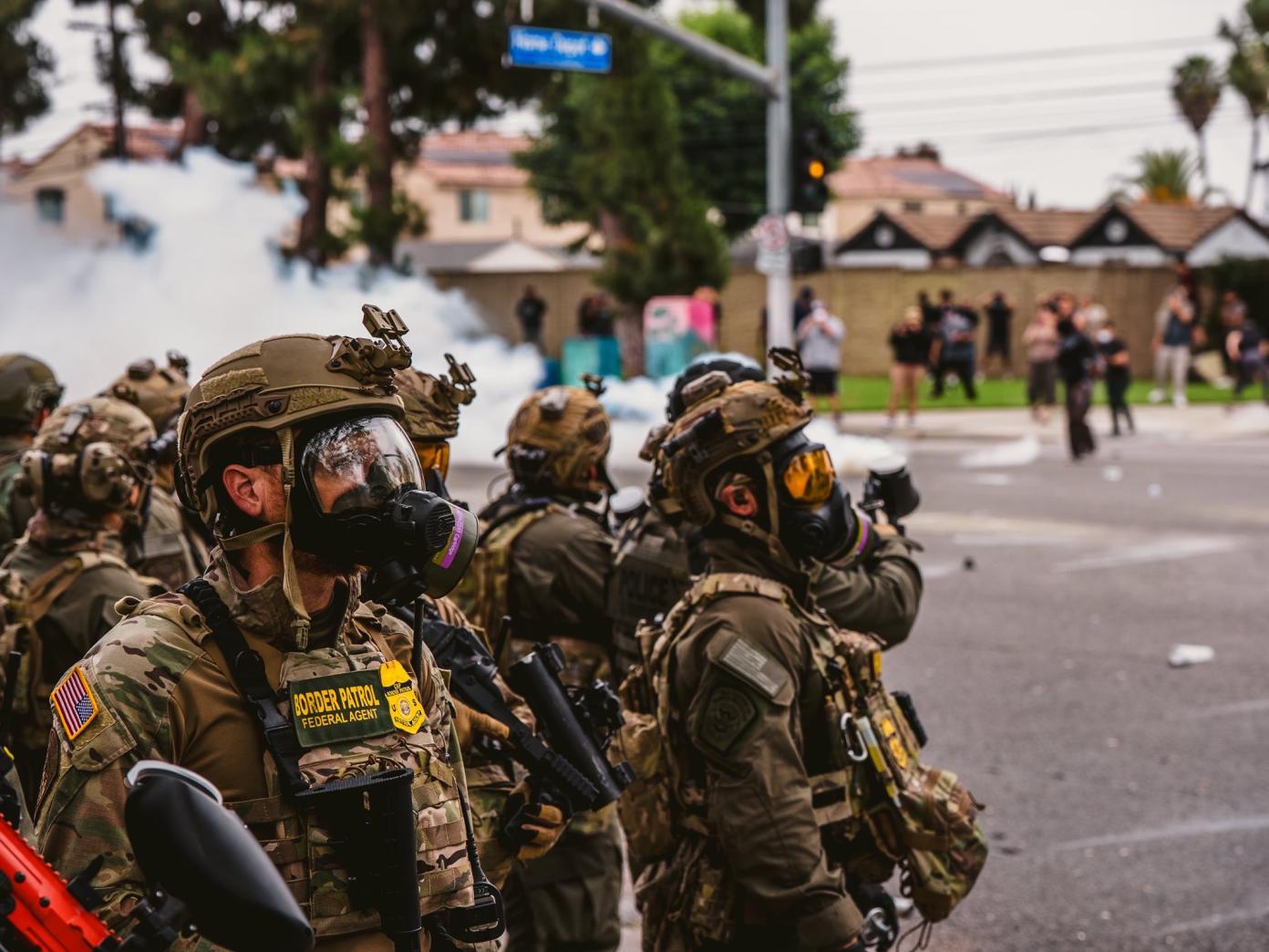 美國邊境巡邏隊（Border Patrol）人員身穿防暴裝備、頭戴防毒面具站崗並施放催淚瓦斯。翻攝美國邊境巡邏隊X